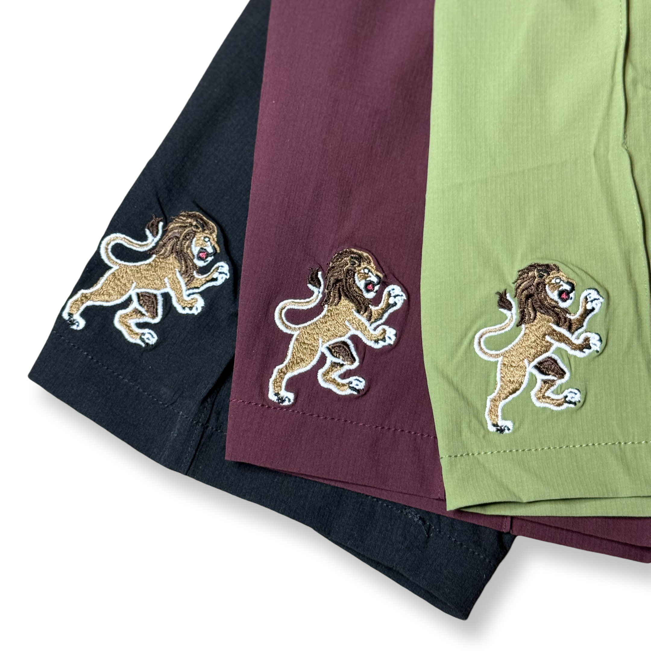 Lightweight cropped pants in Camouflage Green by Lion’s Tale Studios — modern fit, breathable nylon-spandex blend, bold lion emblem on the leg, branded buttons, unisex style for gym or smart casual wear. Lichtgewicht cropped broek in Camouflage Green van Lion’s Tale Studios — moderne pasvorm, ademende nylon-spandex mix, brullend leeuw-embleem op het been, merkknopen, uniseks stijl voor sport of casual chic.