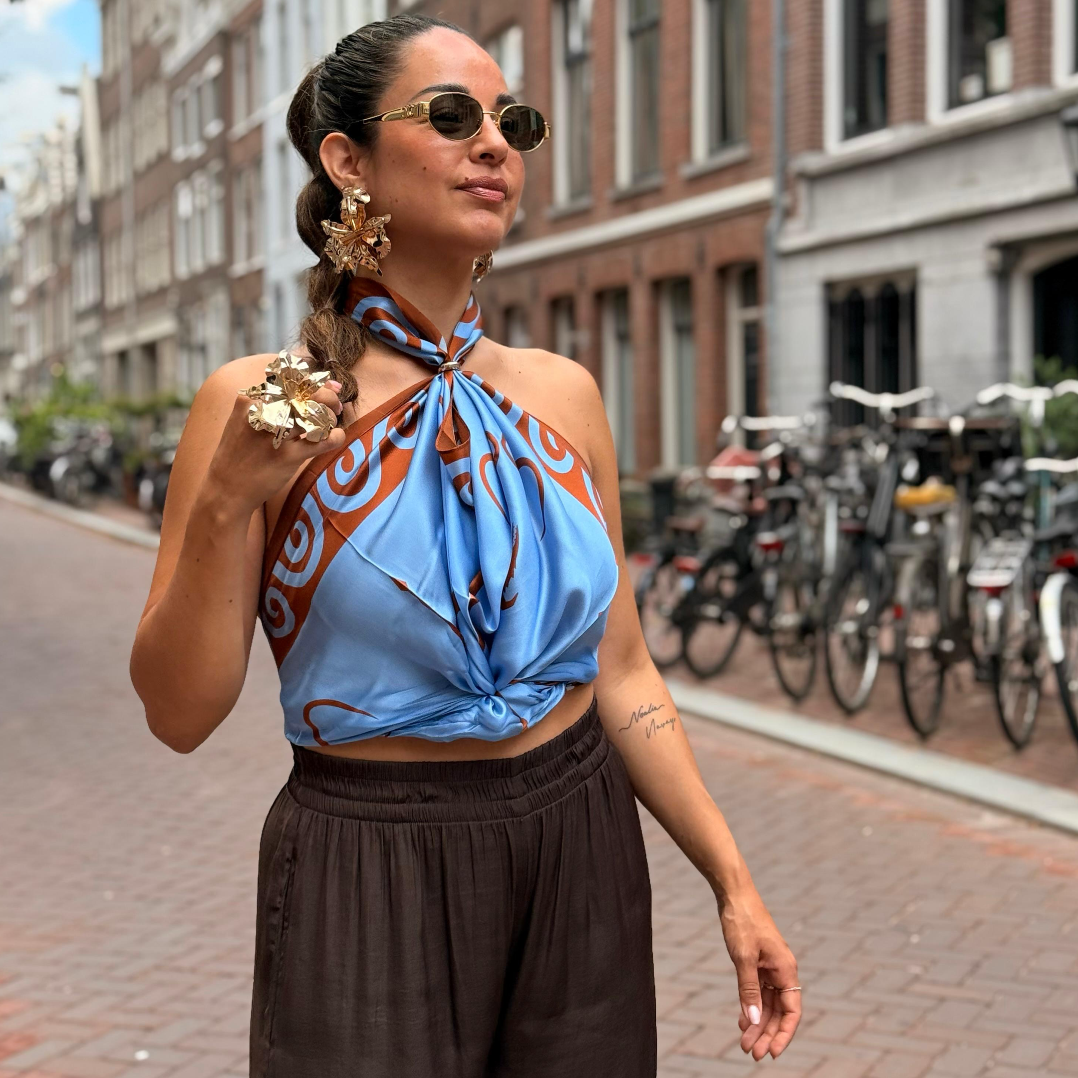 model wearing a 100% pure silk scarf by Lion’s Tale Studios luxury babushka wrap with Moluccan ancestral symbols, cream and oxford blue design, hypoallergenic and breathable silk, styled for unisex minimalist fashion and heritage streetwear. Vrouwelijk model met tattoos draagt een 100% zijden sjaal van Lion’s Tale Studios luxe babushka-stijl met Molukse symbolen, crème en oxfordblauw ontwerp, hypoallergeen en ademend, geschikt voor uniseks mode en erfgoed-geïnspireerde stijl. faline ramirez Amsterdam