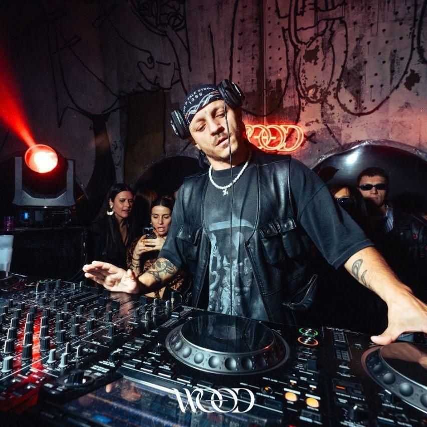 DJ Producer Party Lion's Tale Studios 001 Wood Club Official 2025 100% cotton scarf with batik/paisley print by Lion’s Tale Studios square black, grey, and brown design with 'Pahlawan' logo meaning warrior. Can be styled as scarf or babushka. Worn by Chiara Patawala and Reelow. 100% katoenen sjaal met batik/paisley print van Lion’s Tale Studios — vierkante sjaal in zwart, grijs en bruin met ‘Pahlawan’-logo dat krijger betekent. Draagbaar als sjaal of babushka.